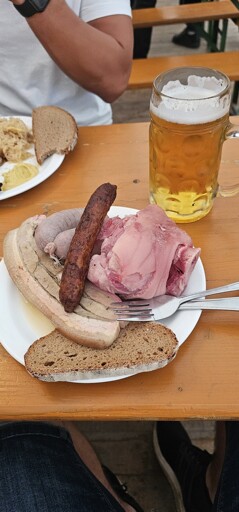 A plate with a single slice of bread with an ungodly amount of horrible looking meat on top. There is a slice of really grey boiled porkbelly. A even greyer boiled sausage which kinda looks like a naked rat. Also a big chunk of boiled corned ham hook and at last a grilled sausage on top which looks kinda decent but could be mistaken as a turd throning over the rest. 